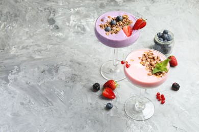 Photo of Different tasty yogurts with fresh berries and granola in glasses on gray textured table, space for text