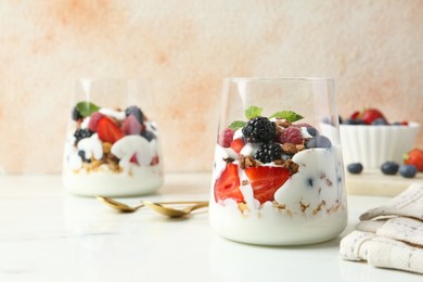 Photo of Tasty yogurt with fresh berries, granola and mint in glasses served on white table