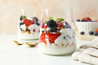 Photo of Tasty yogurt with fresh berries, granola and mint in glasses served on white table