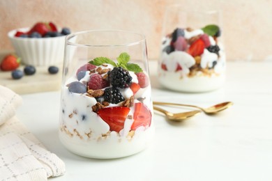 Photo of Tasty yogurt with fresh berries, granola and mint in glasses served on white table