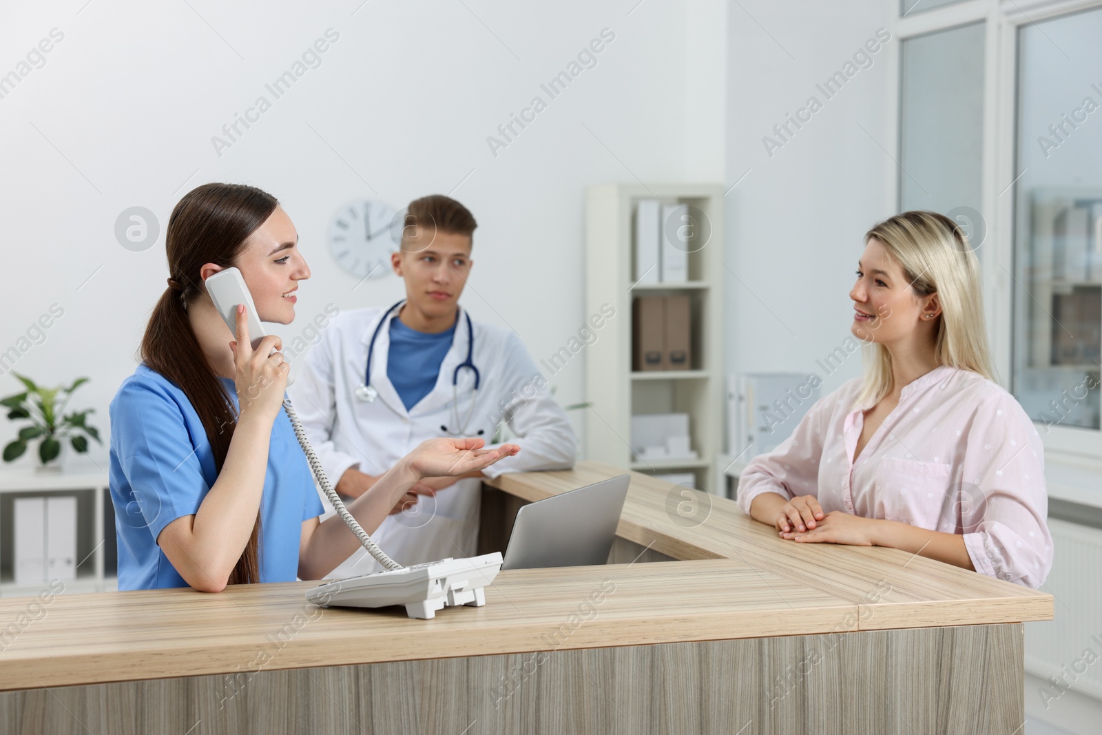 Photo of Professional receptionist and doctor working with patient at wooden desk in hospital