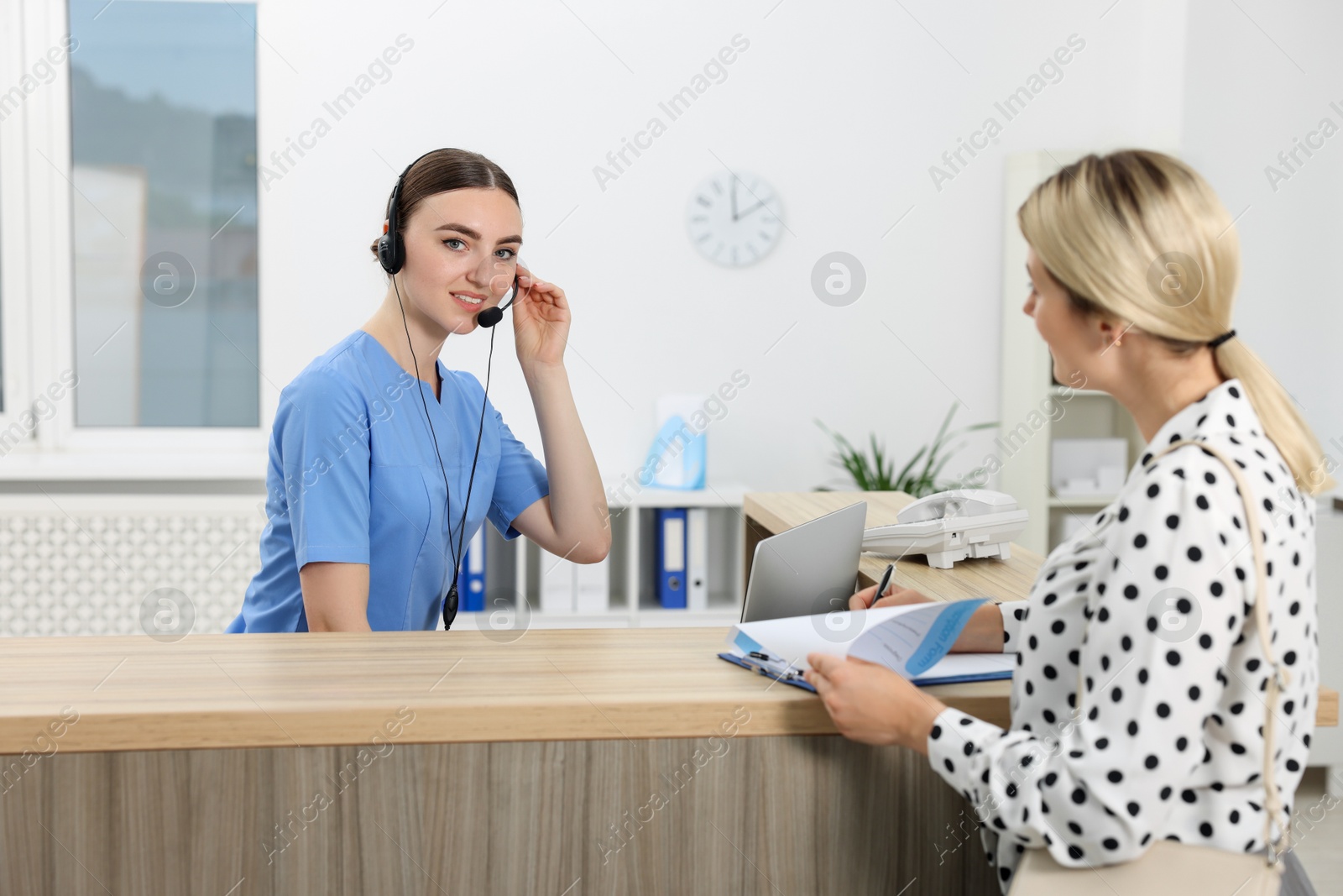 Photo of Professional receptionist working with patient at wooden desk in hospital