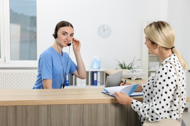 Professional receptionist working with patient at wooden desk in hospital