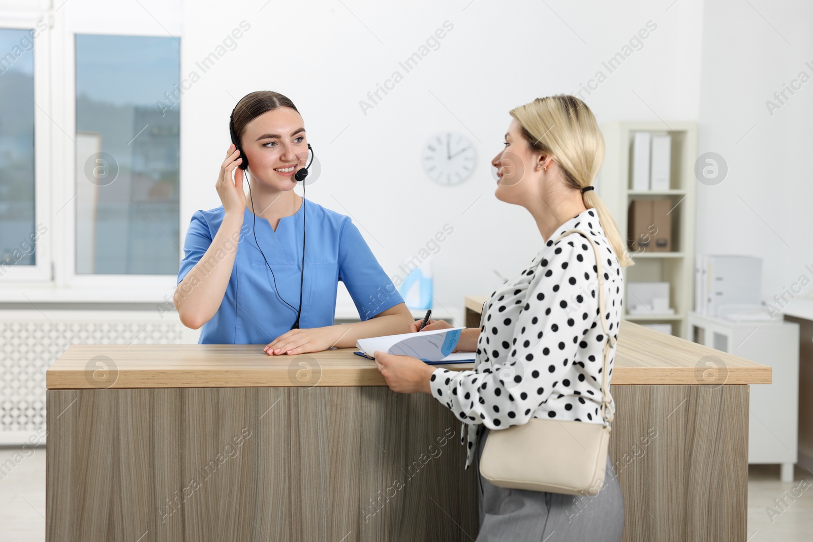 Photo of Professional receptionist working with patient at wooden desk in hospital