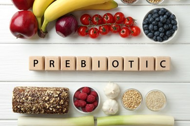 Photo of Word Prebiotic made of cubes and different products on white wooden table, flat lay