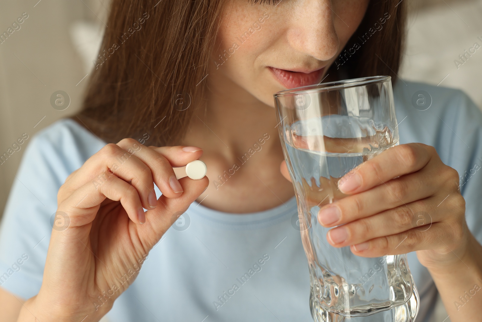 Photo of Woman with glass of water taking pill at home, closeup