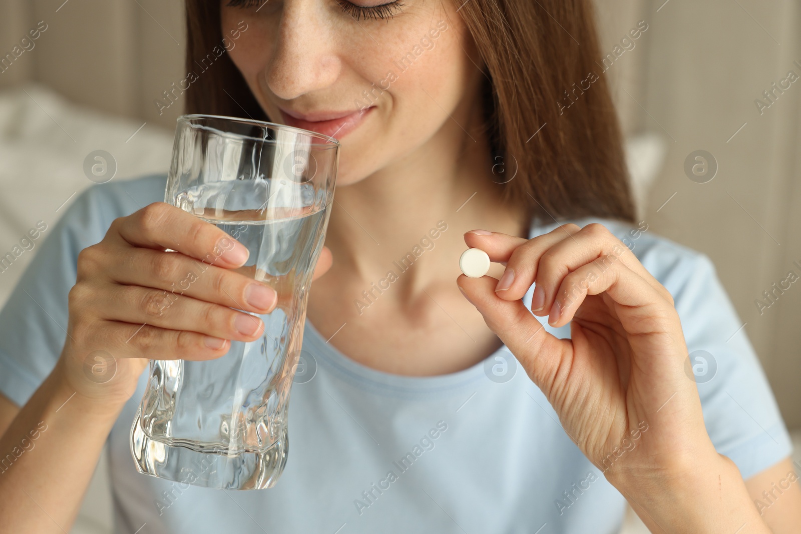 Photo of Woman with glass of water taking pill indoors, closeup