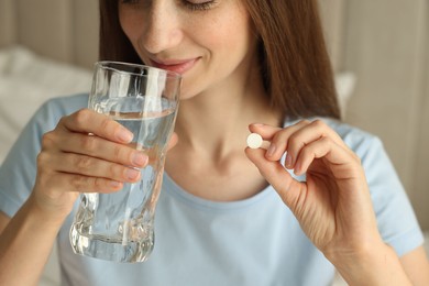 Photo of Woman with glass of water taking pill indoors, closeup