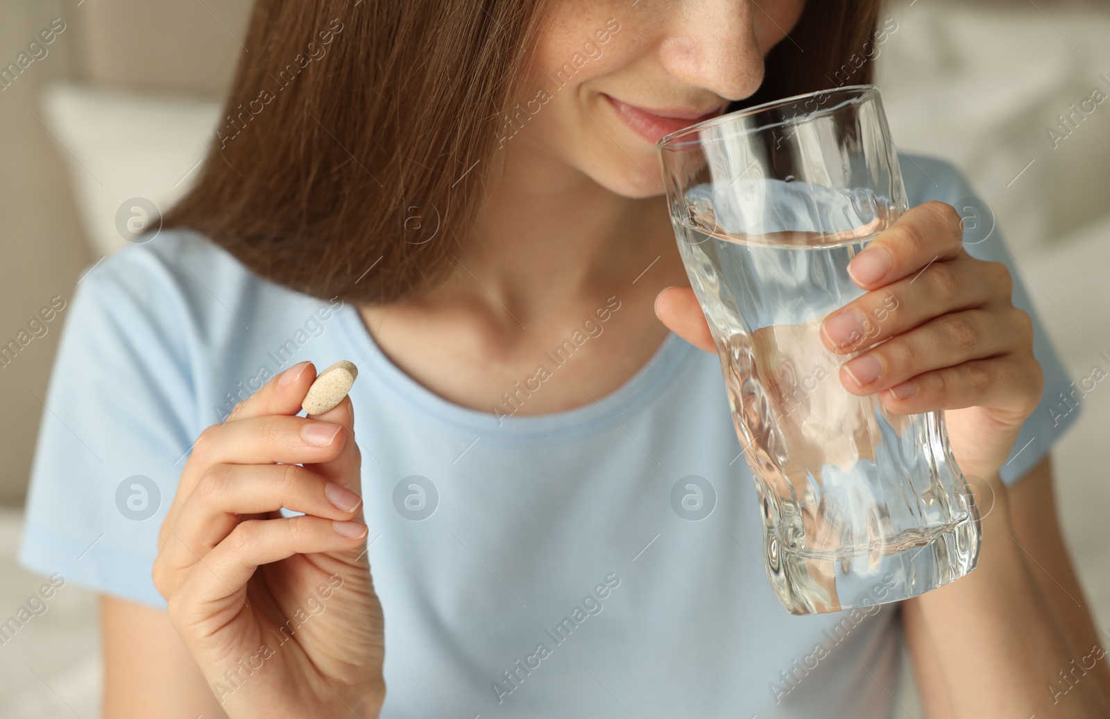 Photo of Woman with glass of water taking pill at home, closeup