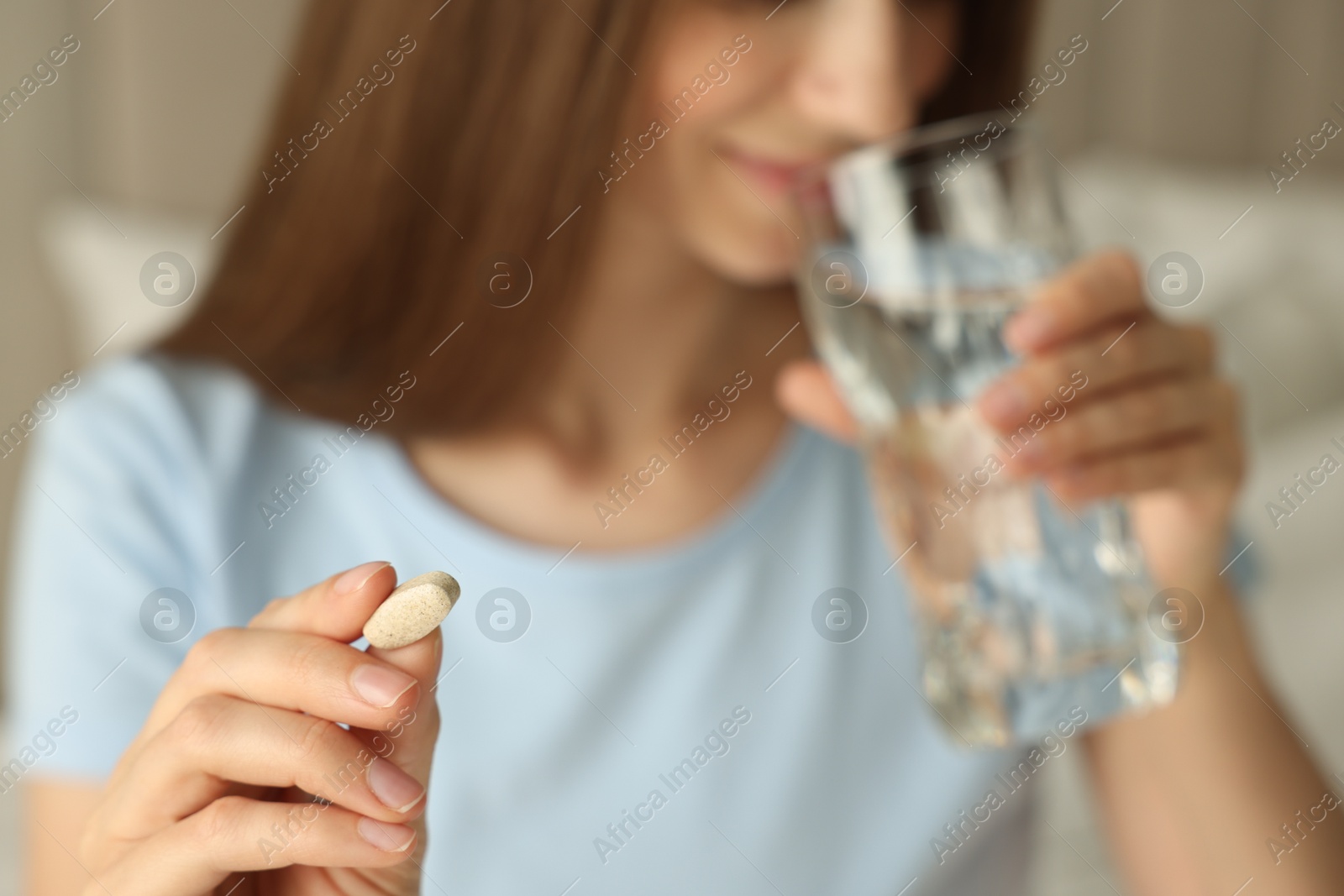 Photo of Woman with glass of water taking pill indoors, closeup