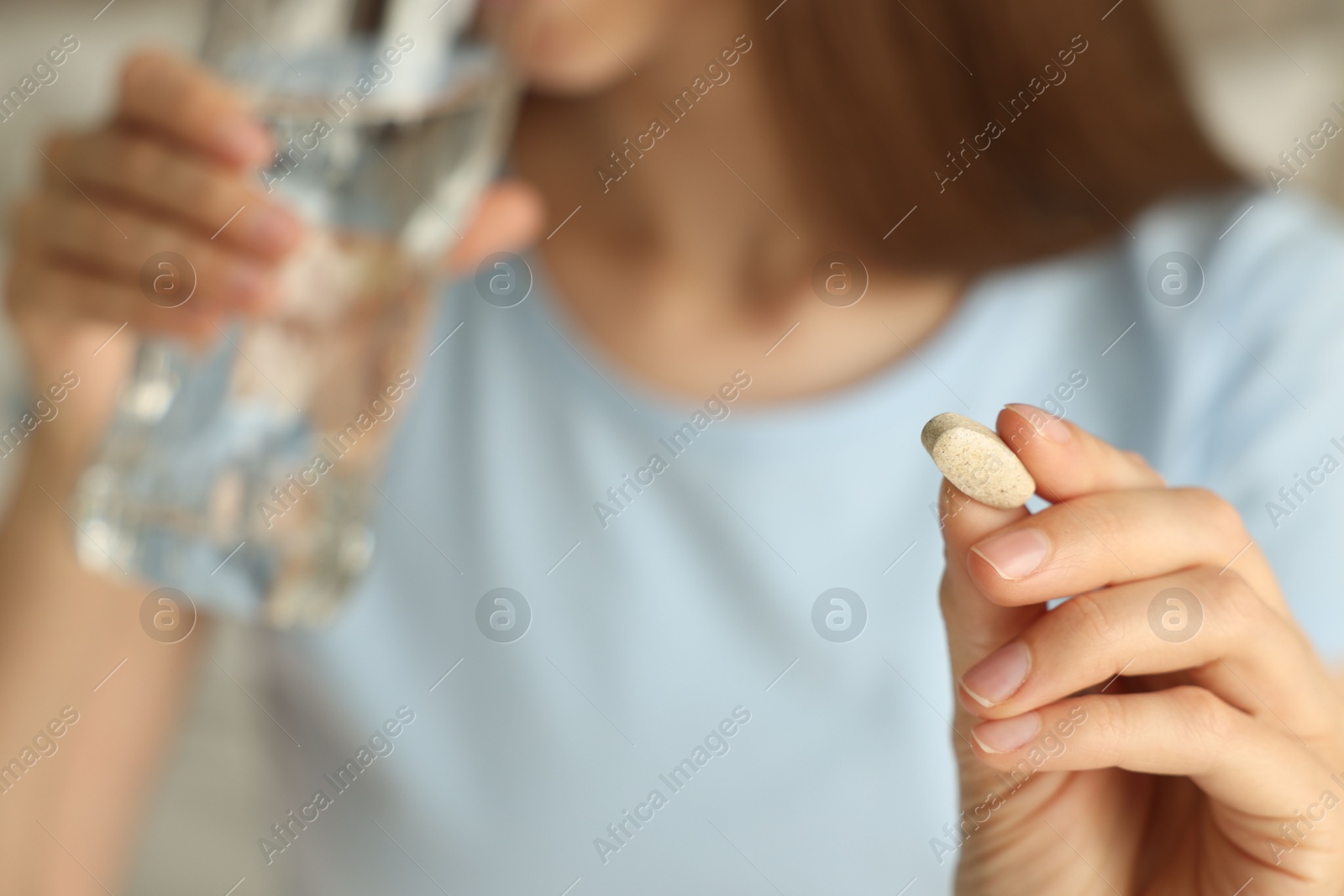 Photo of Woman with glass of water taking pill indoors, closeup