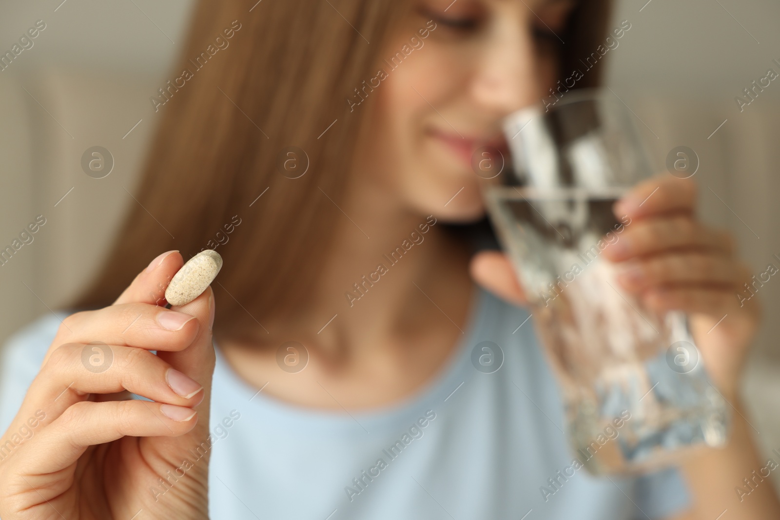 Photo of Woman with glass of water taking pill indoors, selective focus