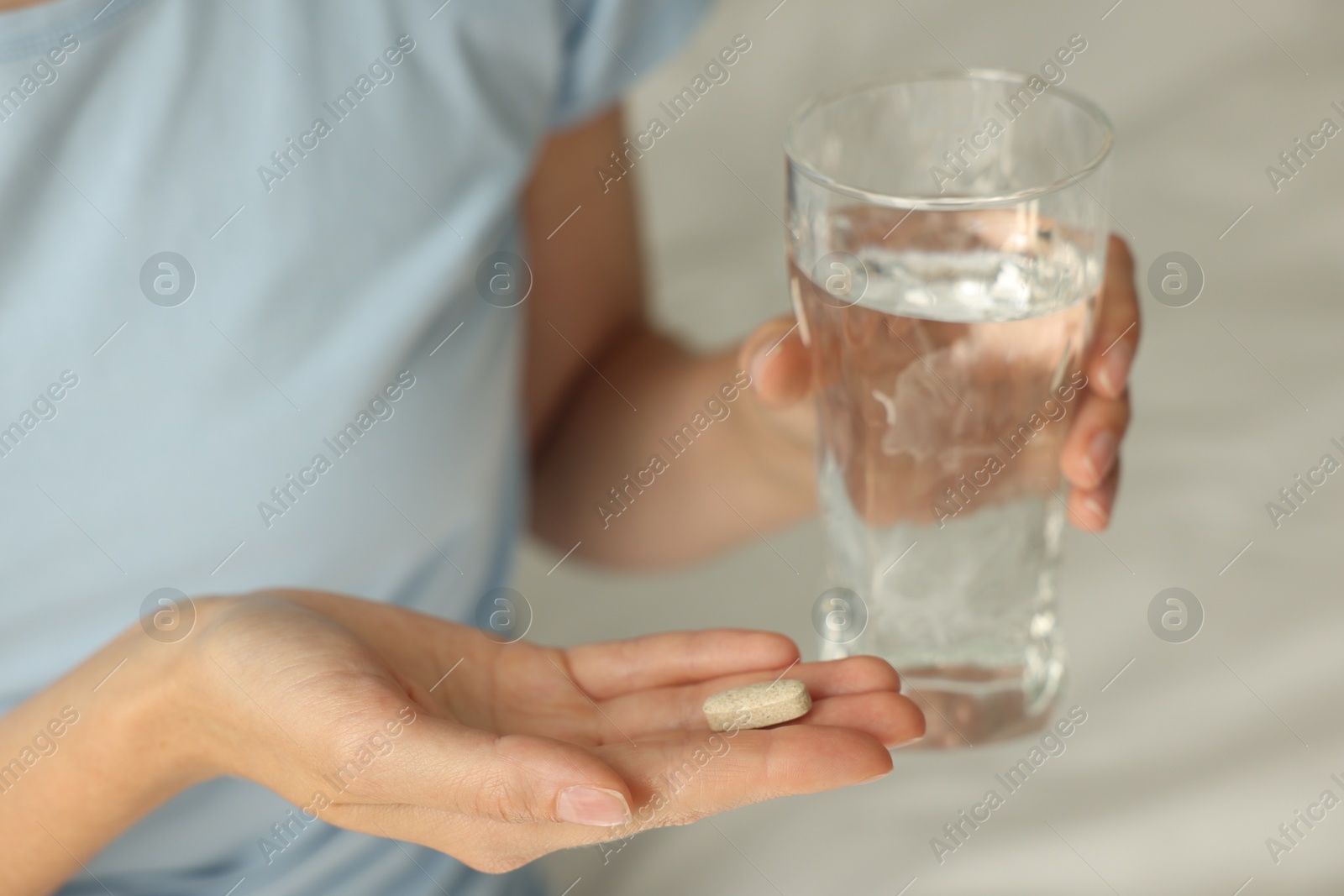 Photo of Woman with glass of water and pill indoors, closeup