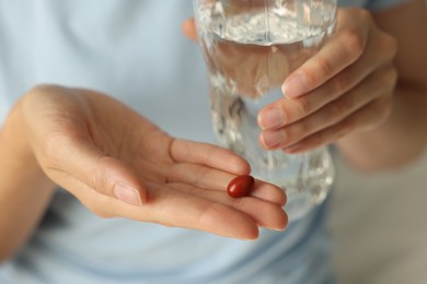 Woman with glass of water and pill indoors, closeup