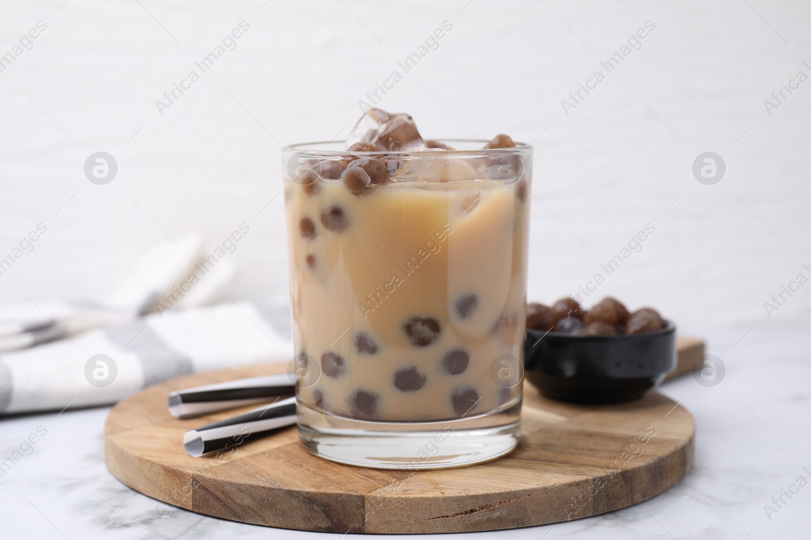 Photo of Tasty milk bubble tea in glass, tapioca pearls and straws on white marble table