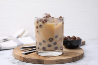 Tasty milk bubble tea in glass, tapioca pearls and straws on white marble table