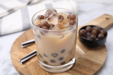 Tasty milk bubble tea in glass, tapioca pearls and straws on white marble table, closeup