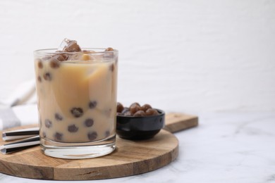 Tasty milk bubble tea in glass, tapioca pearls and straws on white marble table, space for text