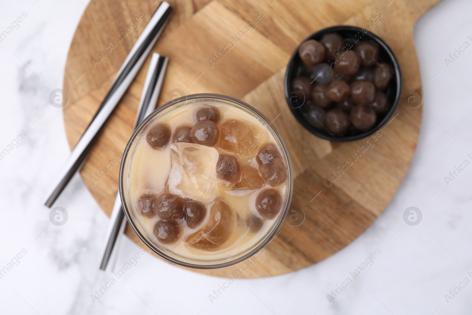 Photo of Tasty milk bubble tea in glass, tapioca pearls and straws on white marble table, top view