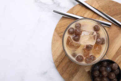 Photo of Tasty milk bubble tea in glass, tapioca pearls and straws on white marble table, top view. Space for text