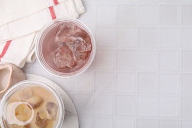 Photo of Tasty bubble tea in plastic cups on white tiled table, top view. Space for text