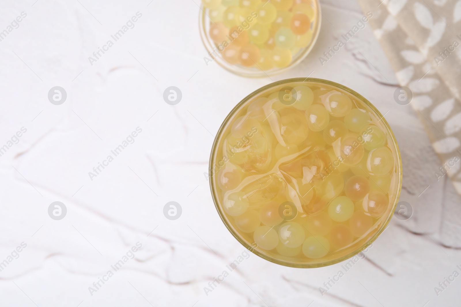 Photo of Tasty bubble tea in glass and tapioca pearls on white table, top view. Space for text