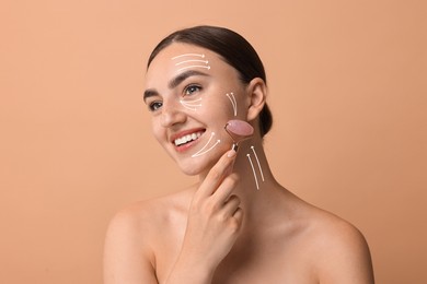 Beautiful young woman doing facial massage with roller on dark beige background. Lines on skin showing directions of motion