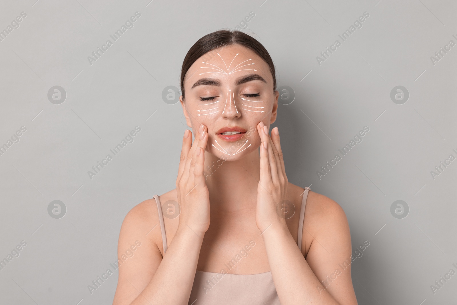 Image of Beautiful young woman doing face massage with fingers on grey background. Lines on skin showing directions of motion