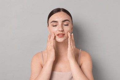 Beautiful young woman doing face massage with fingers on grey background. Lines on skin showing directions of motion