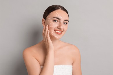 Beautiful young woman doing face massage with fingers on grey background. Lines on skin showing directions of motion