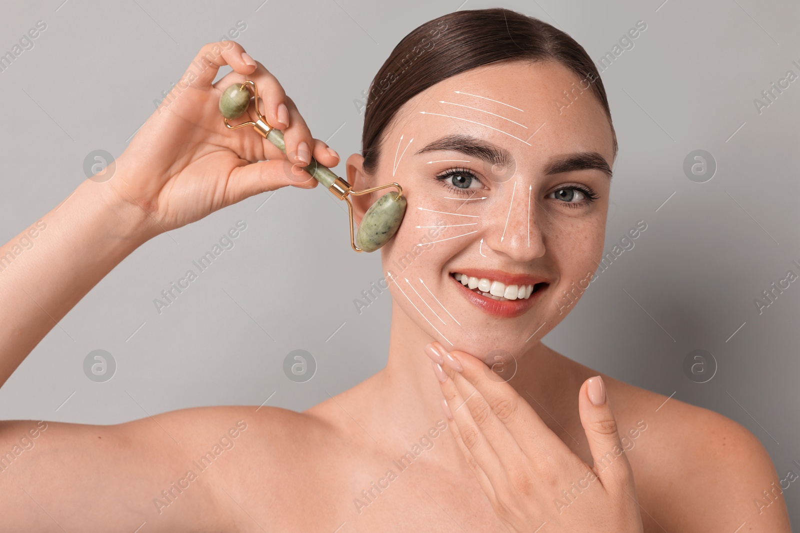 Image of Beautiful young woman doing facial massage with roller on grey background. Lines on skin showing directions of motion