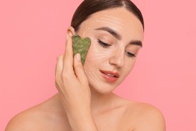 Image of Beautiful young woman doing facial massage with gua sha tool on pink background. Lines on skin showing directions of motion