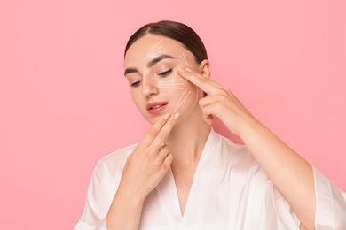 Beautiful young woman doing face massage with fingers on pink background. Lines on skin showing directions of motion