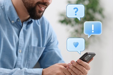 Happy man sending message via smartphone at home, closeup. Speech bubbles near device