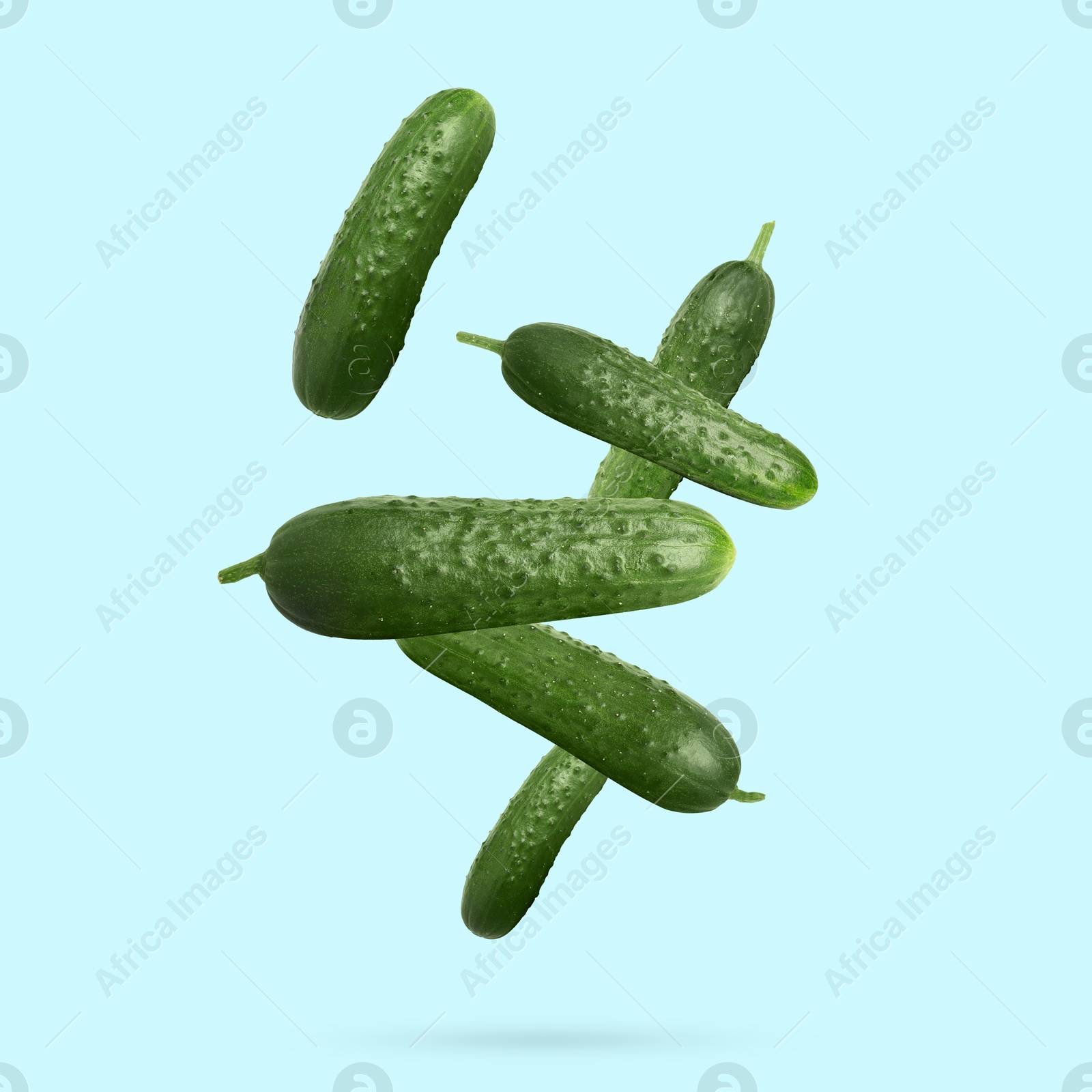 Image of Whole ripe cucumbers falling on light blue background