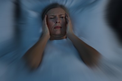 Senior woman suffering from headache in bed, motion blur effect