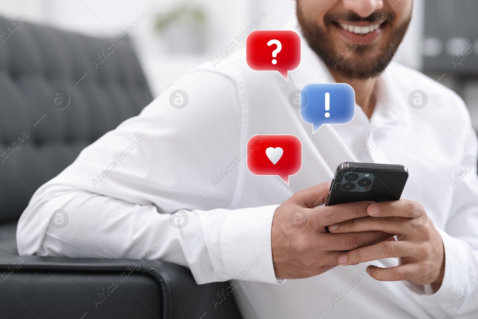 Image of Happy man sending message via smartphone at home, closeup. Speech bubbles near device