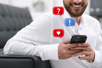 Image of Happy man sending message via smartphone at home, closeup. Speech bubbles near device