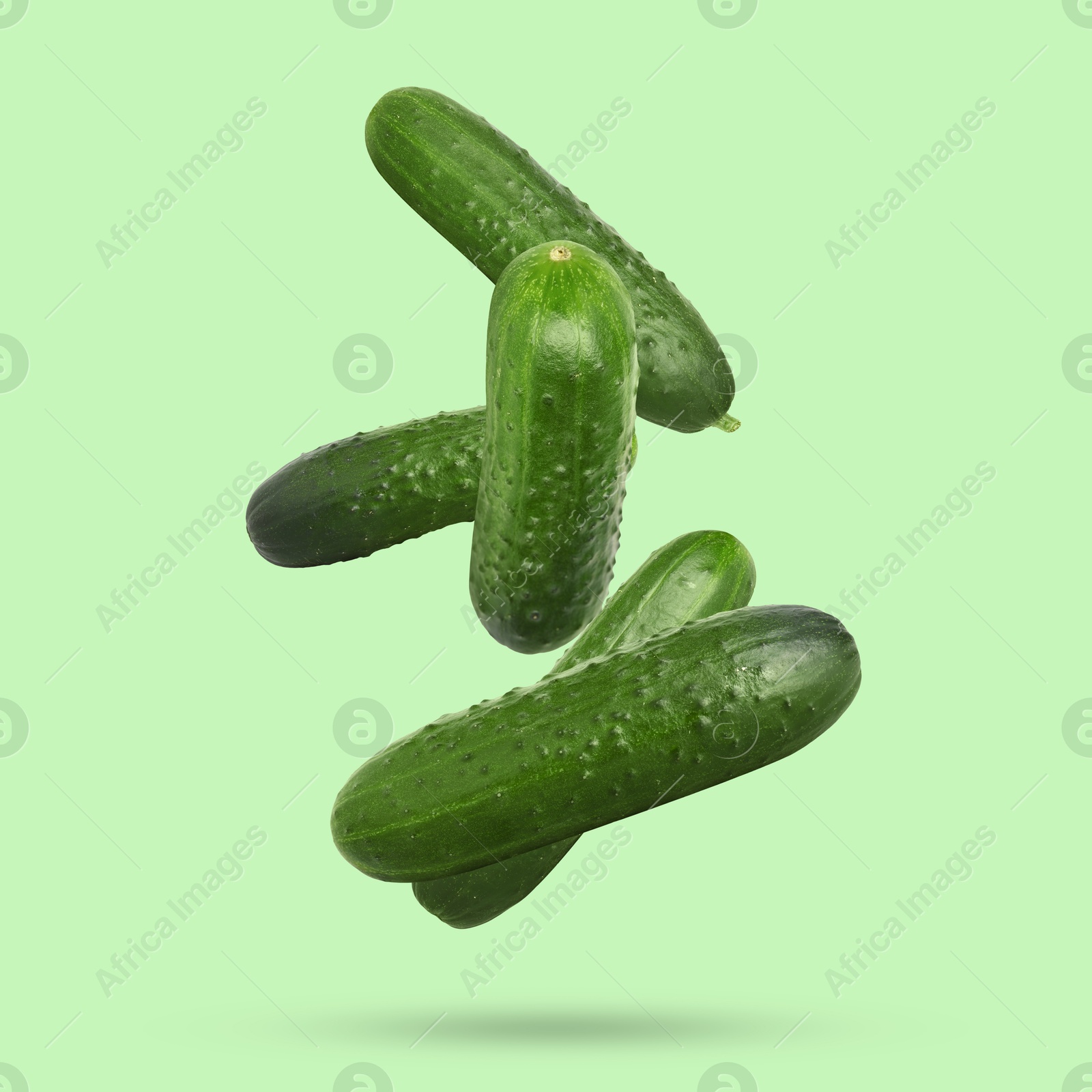 Image of Whole ripe cucumbers falling on green background