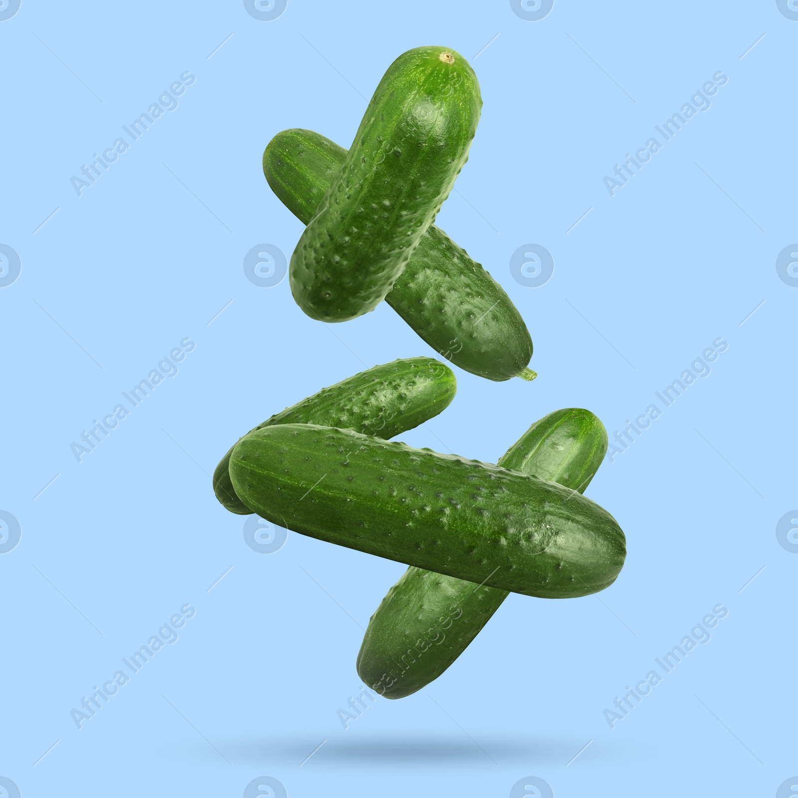 Image of Whole ripe cucumbers falling on light blue background