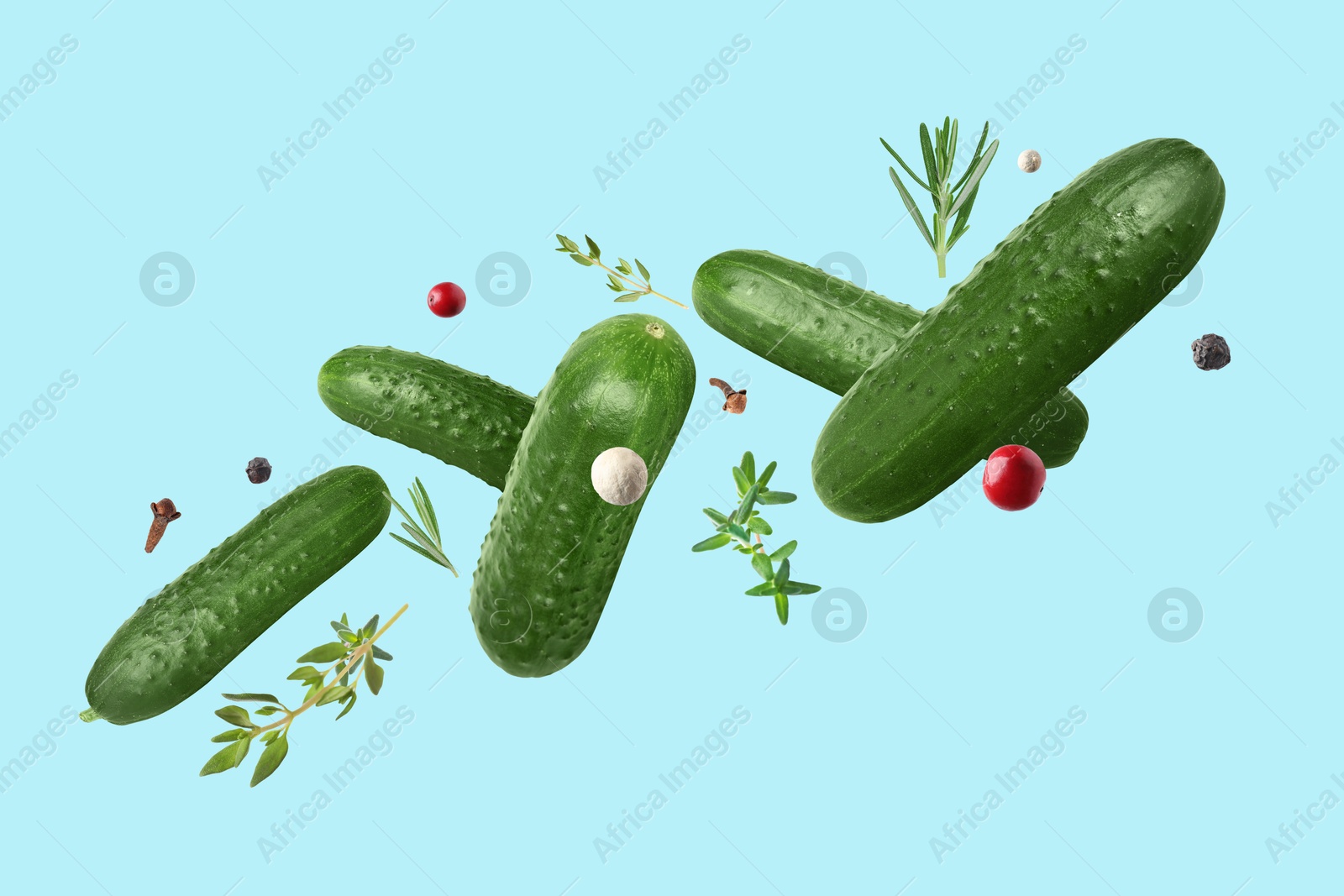 Image of Ripe cucumbers, herbs and spices falling on light blue background