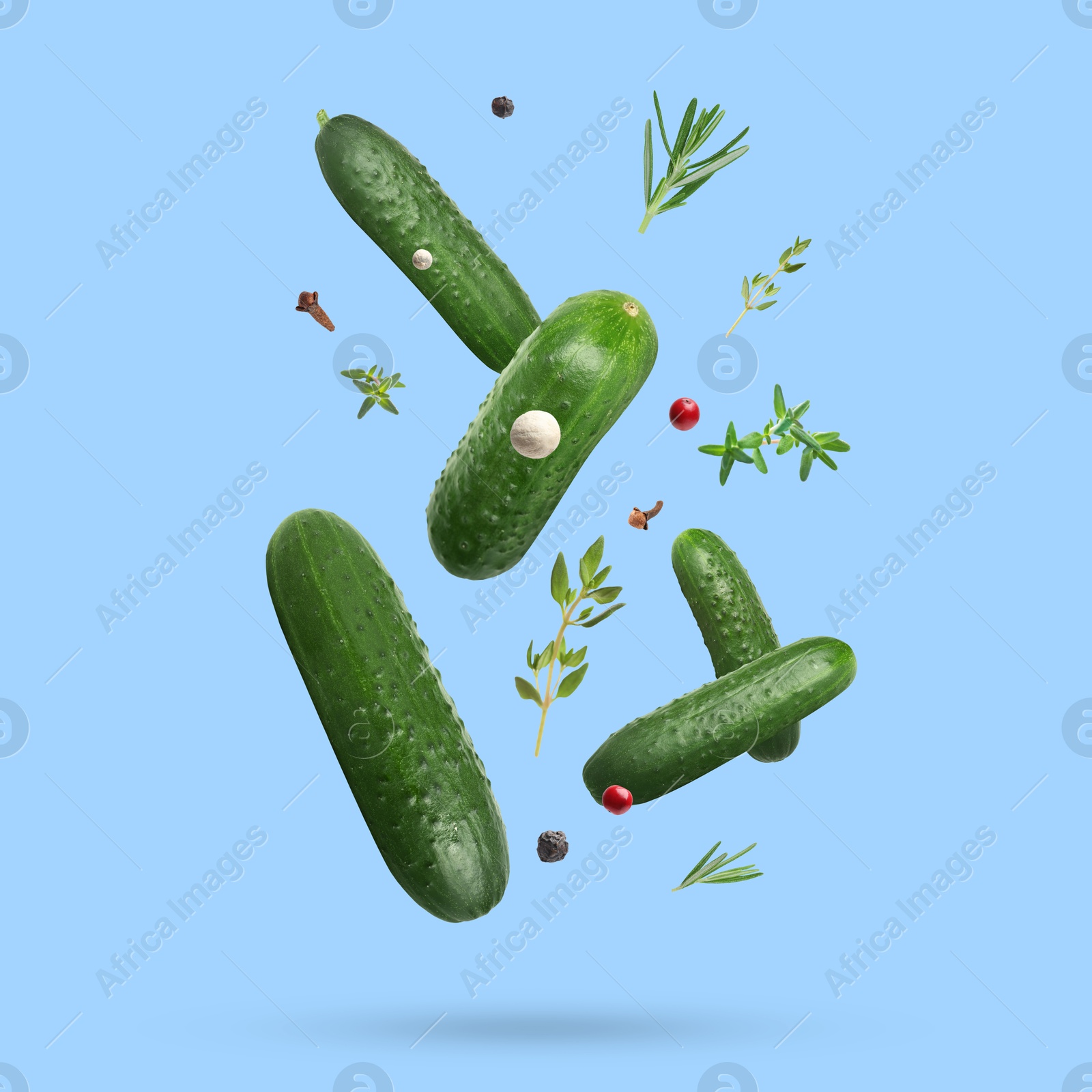 Image of Ripe cucumbers, herbs and spices falling on light blue background