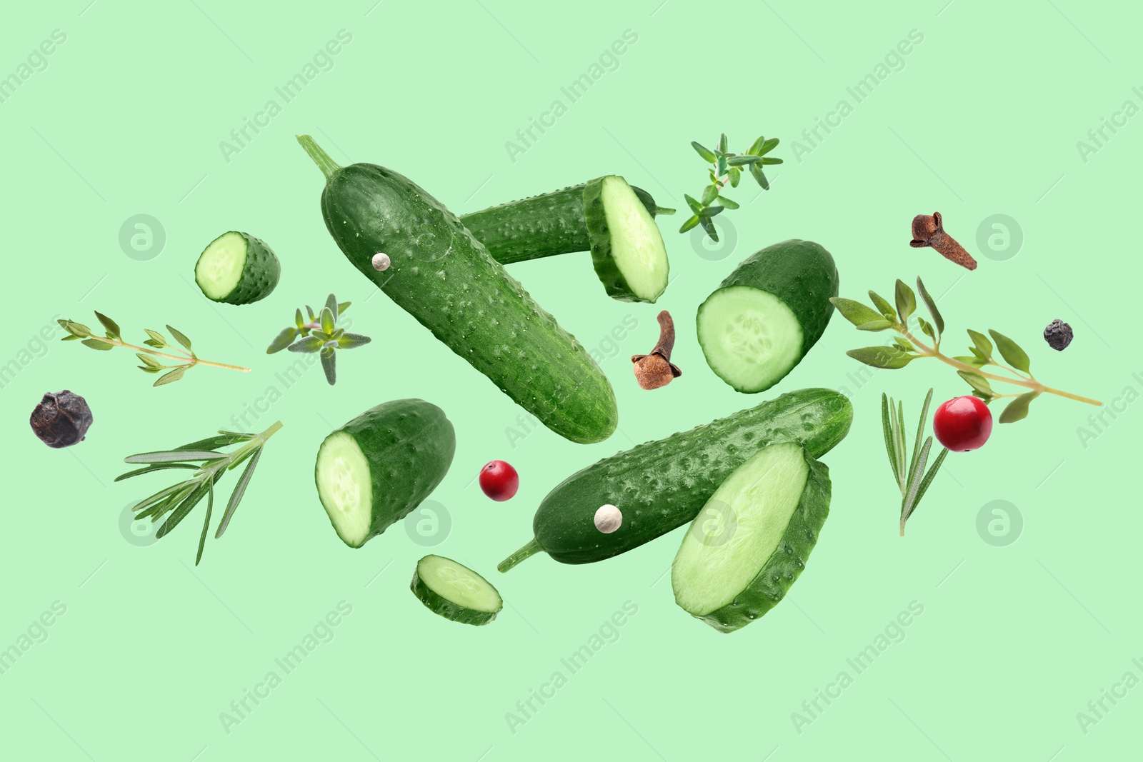 Image of Ripe cucumbers, herbs and spices flying on light green background