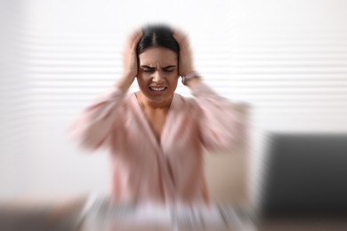 Woman suffering from headache indoors, motion blur effect