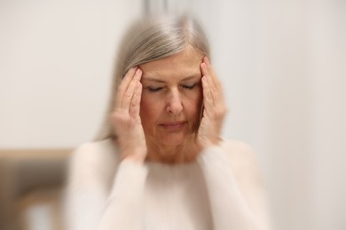 Senior woman suffering from headache indoors, motion blur effect