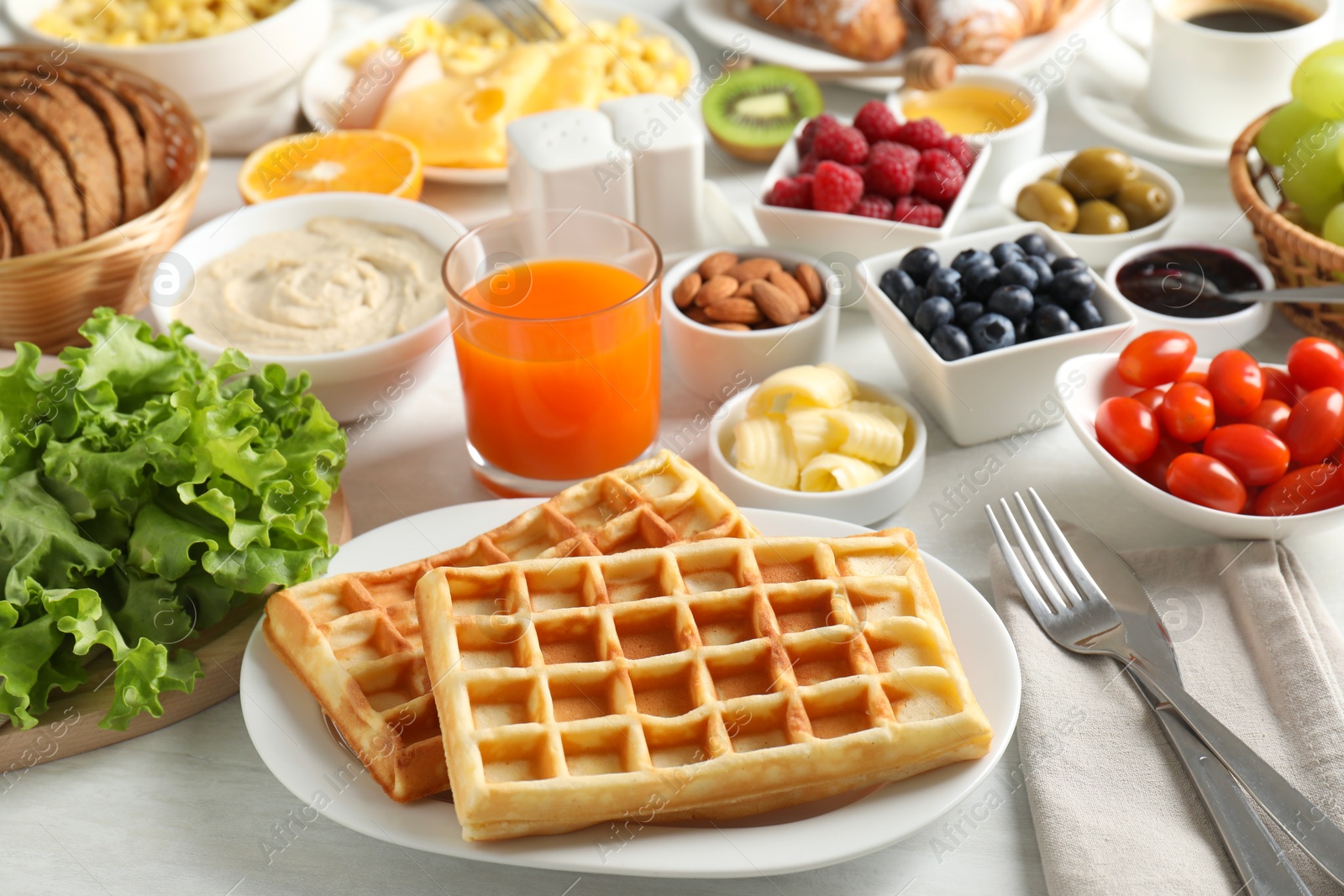 Photo of Tasty breakfast. Belgian waffles, orange juice and other food on light wooden table, closeup