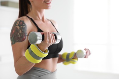 Photo of Woman with ankle weights and dumbbells training indoors, closeup