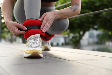 Photo of Woman putting on ankle weights outdoors, closeup