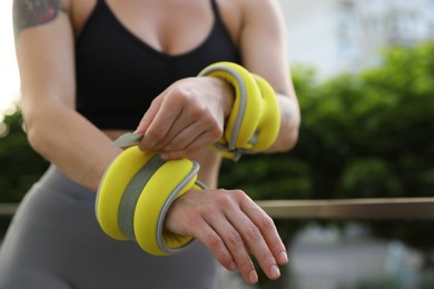 Photo of Woman putting ankle weight on her arm outdoors, closeup