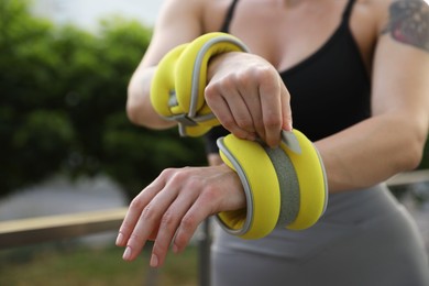 Woman putting ankle weight on her arm outdoors, closeup